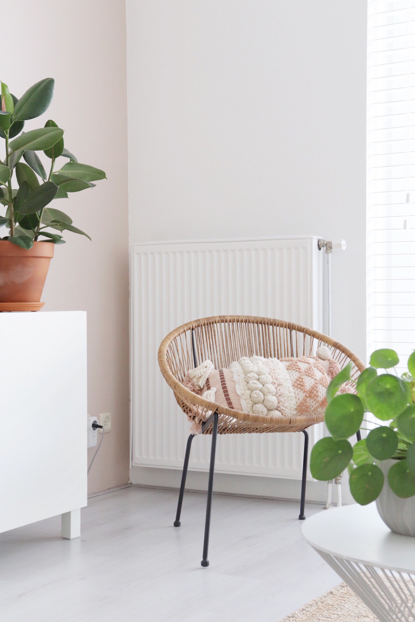 een hoekje in de woonkamer met een rotan stoel, roze accent en twee groene planten.