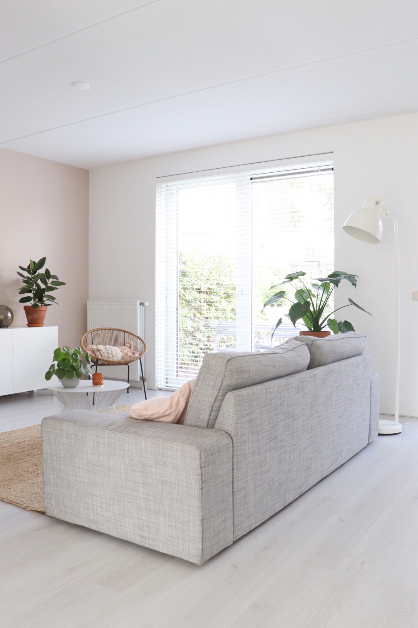de zithoek in de woonkamer met een grijze bank, rotan stoel en planten. 